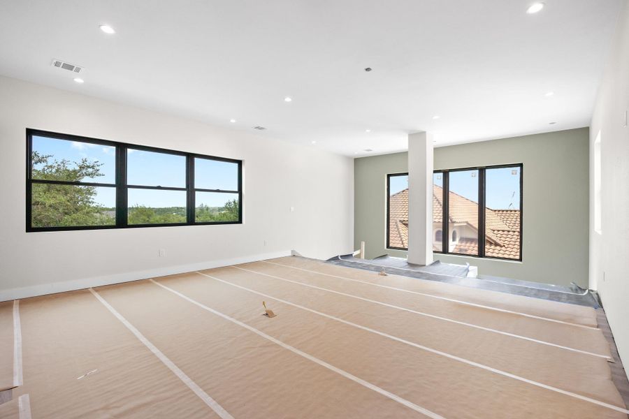 Spacious room featuring multiple large windows with black frames, recessed lighting, and a neutral color palette