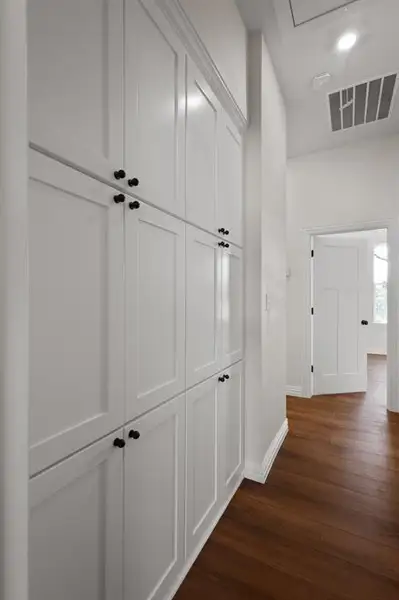 Hall featuring dark wood-type flooring, visible vents, baseboards, and attic access
