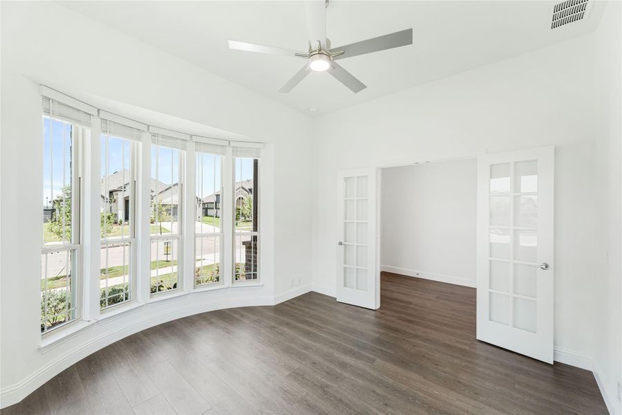 Empty room with bay windows, dark hardwood floors, ceiling fan, and French doors Empty room with bay windows, dark hardwood floors, ceiling fan, and French doors