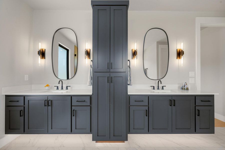 Custom cabinetry divides two elegant vanities on polished stone floors.
