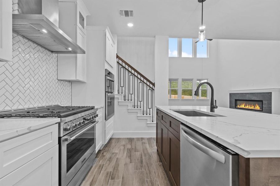 Kitchen featuring sink, hanging light fixtures, stainless steel appliances, white cabinets, and ventilation hood