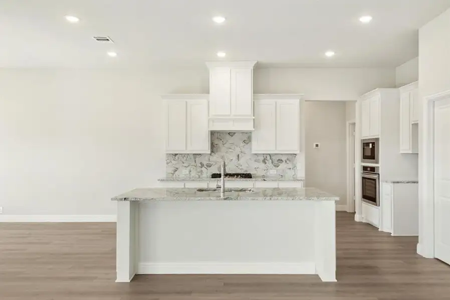 Kitchen featuring a center island with a sink, white cabinetry, integrated stainless steel appliances, a patterned backsplash, and wood-finish flooring Kitchen featuring a center island with a sink, white cabinetry, integrated stainless steel appliances, a patterned backsplash, and wood-finish flooring