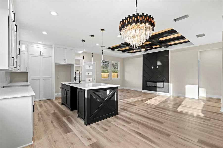 Kitchen featuring sink, an inviting chandelier, pendant lighting, a kitchen island with sink, and white cabinets