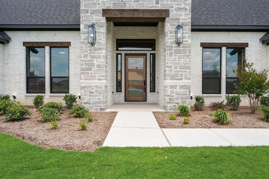 Modern facade featuring a wooden entry door with frosted glass panels, surrounded by a light-toned brick and stone veneer
