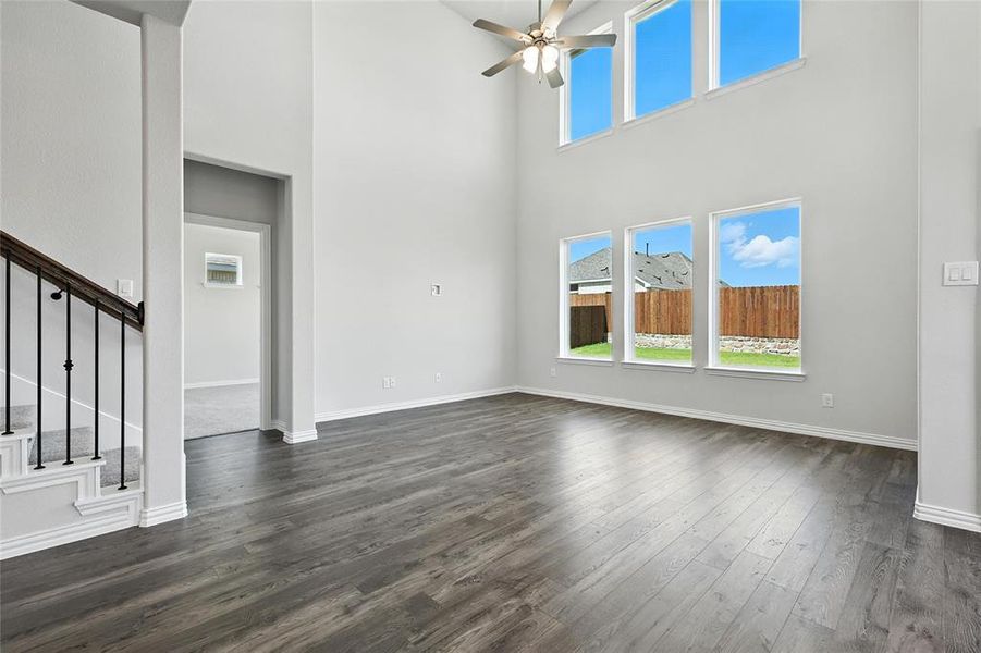 Unfurnished living room with a ceiling fan, dark wood finished floors, and a high ceiling
