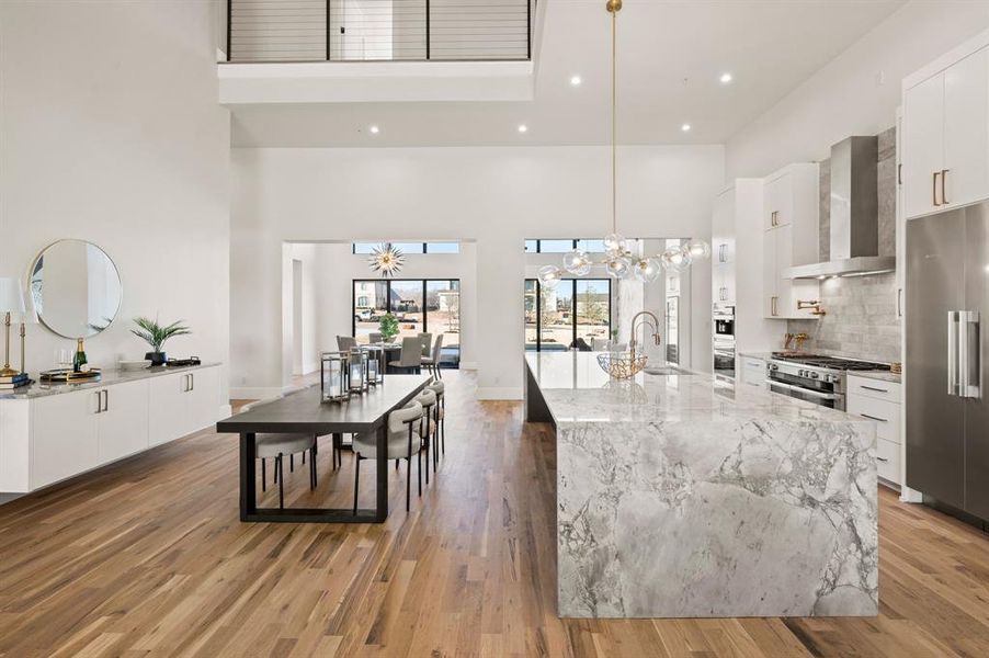 Kitchen featuring high end refrigerator, wall chimney range hood, white cabinets, and decorative light fixtures