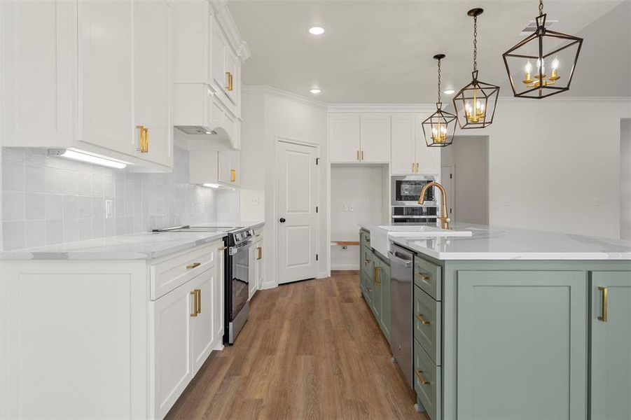 Kitchen with green cabinetry, white cabinetry, ornamental molding, appliances with stainless steel finishes, and an island with sink Kitchen with green cabinetry, white cabinetry, ornamental molding, appliances with stainless steel finishes, and an island with sink