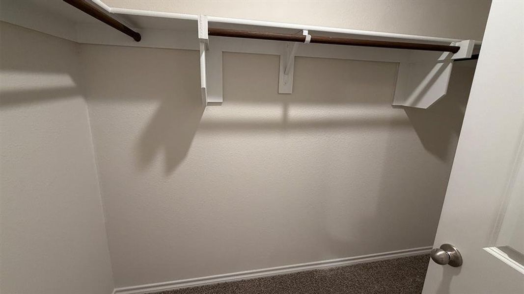 Interior closet featuring a white door with a brushed nickel knob, white shelving, and a dark wood-finish hanging rod