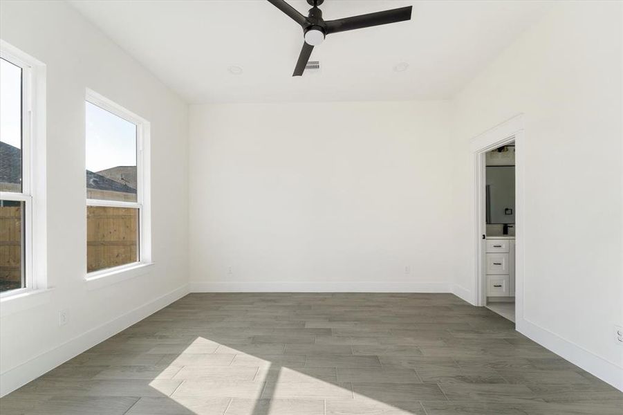 The primary bedroom boasts recessed lighting and a ceiling fan. Enjoy natural light from two windows, sleek wood-like tile flooring, and convenient cable and TV outlets already installed at mount height.