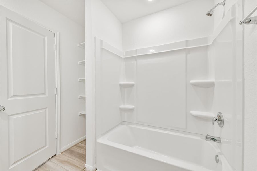 The secondary bathroom showcases a clean white bathtub and shower combination. It features built-in shelving for storage and sleek fixtures. The neutral tones and simple design make it a versatile space.
