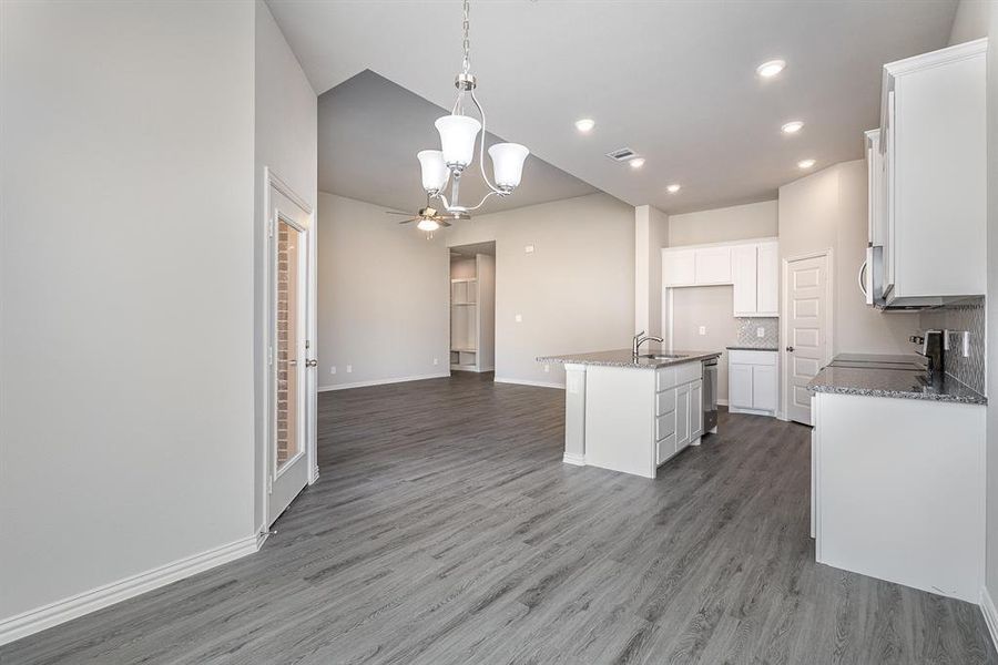 Kitchen featuring pendant lighting, a center island with sink, tasteful backsplash, white cabinetry, and wood-type flooring