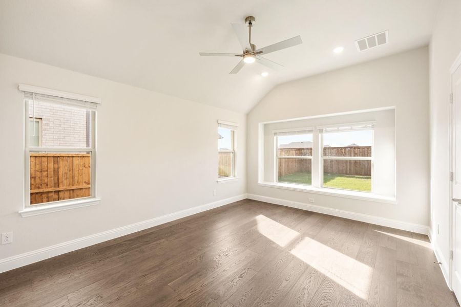 Empty bedroom with vaulted ceiling, ceiling fan, hardwood floors, and large windows overlooking backyard Empty bedroom with vaulted ceiling, ceiling fan, hardwood floors, and large windows overlooking backyard