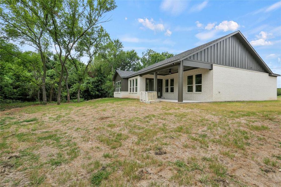 Rear view of property featuring board and batten siding, a ceiling fan, a patio area, brick siding, and a lawn