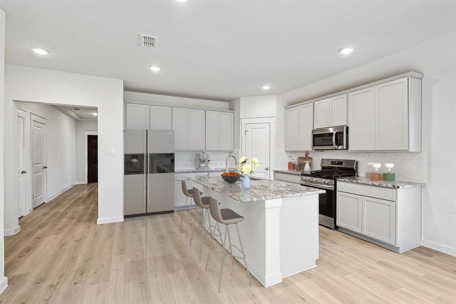 Kitchen featuring light hardwood / wood-style flooring, a kitchen island with sink, stainless steel appliances, and light stone counters