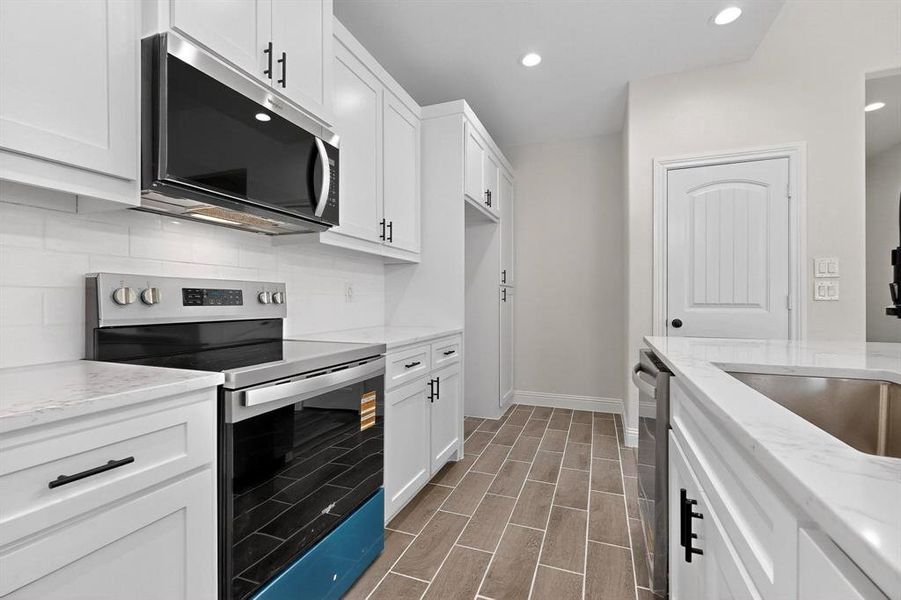 Kitchen featuring stainless steel appliances, backsplash, white cabinetry, recessed lighting, and light stone countertops Kitchen featuring stainless steel appliances, backsplash, white cabinetry, recessed lighting, and light stone countertops