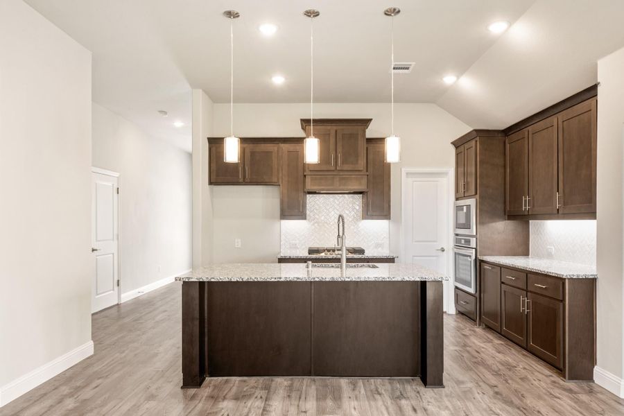 Kitchen with dark wood cabinets, granite island, pendant lights, and light hardwood floors