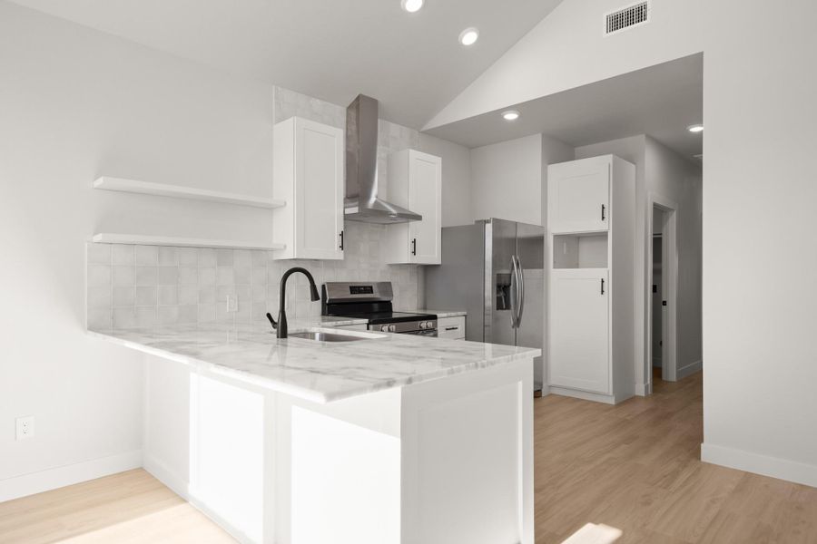 Kitchen with backsplash, vaulted ceiling, a peninsula, light stone counters, and stainless steel appliances