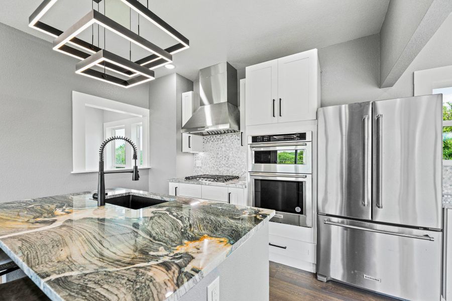 Kitchen island with a waterfall edge countertop, integrated sink, and modern pendant lighting