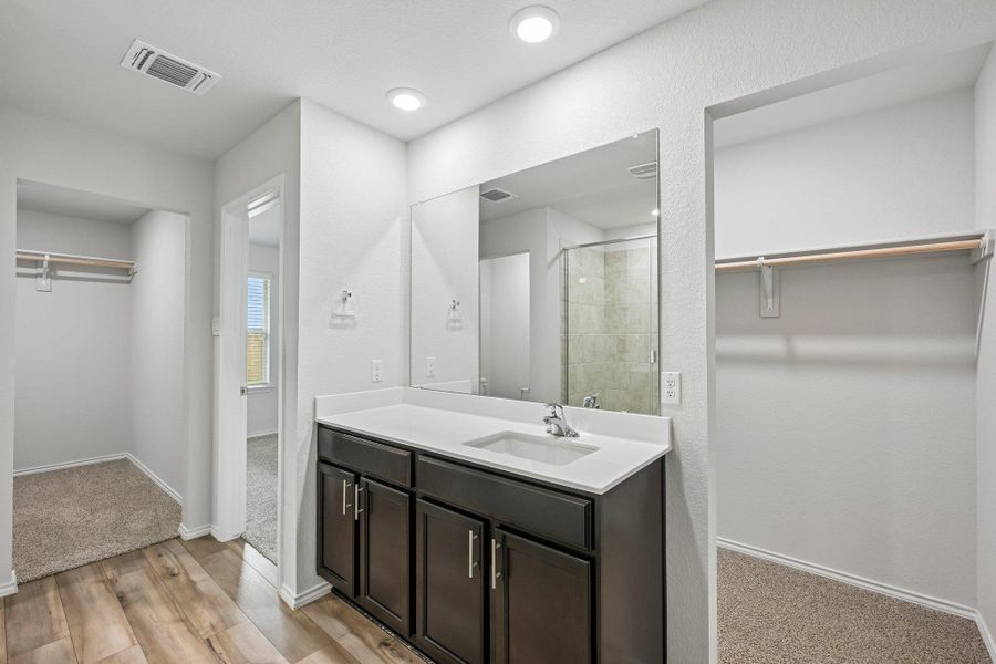 Bathroom vanity featuring a single basin sink, white countertop, and dark wood-finish cabinetry