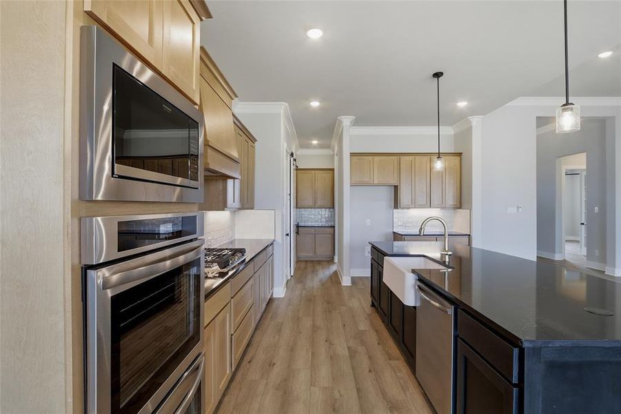 Two tone kitchen featuring stainless steel appliances, light wood-type flooring, a kitchen island with sink, dark stone counters, and pendant lighting