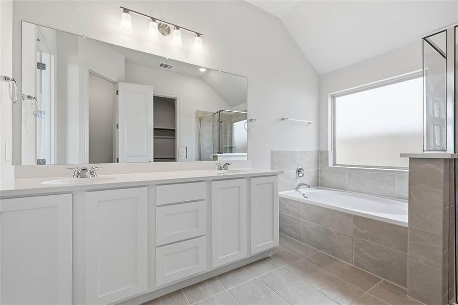 Bathroom with double vanity, a stall shower, a bath, lofted ceiling, and light tile patterned flooring