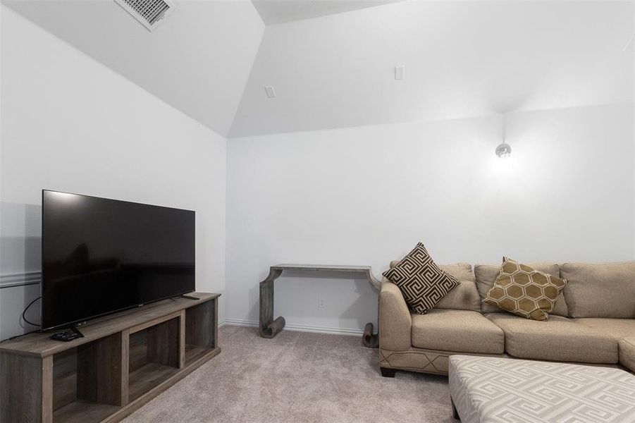 Carpeted living area featuring vaulted ceiling and baseboards