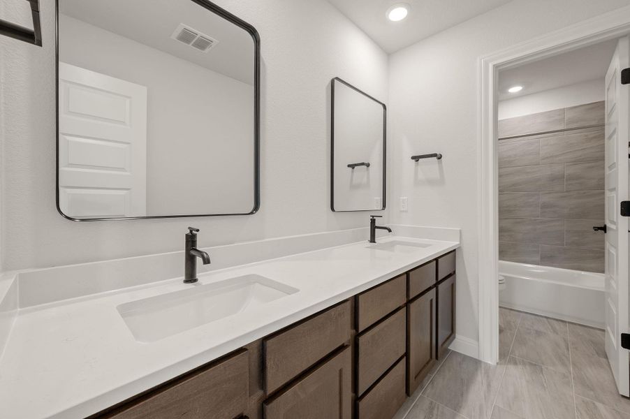 Secondary bathroom featuring dual vanity with tons of storage space and privacy door leading to shower/tub combo