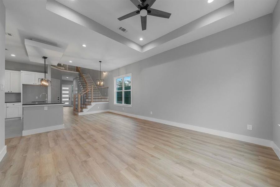 Unfurnished living room featuring baseboards, stairway, light wood-type flooring, a tray ceiling, and ceiling fan with notable chandelier