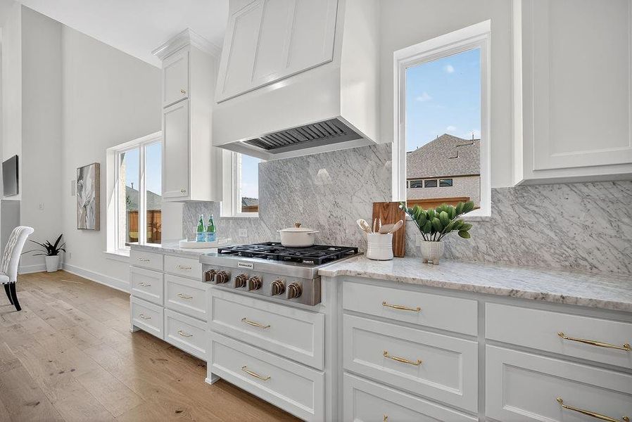 Kitchen with white cabinets, light wood-style flooring, light stone countertops, custom range hood, and tasteful backsplash Kitchen with white cabinets, light wood-style flooring, light stone countertops, custom range hood, and tasteful backsplash