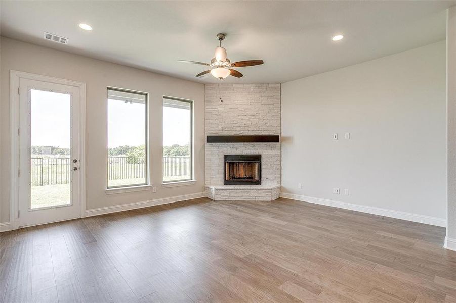 Unfurnished living room with ceiling fan, a stone fireplace, and light hardwood / wood-style flooring