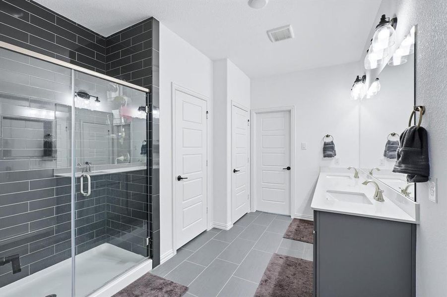 Bathroom with double vanity, a shower stall, and dark tile patterned floors