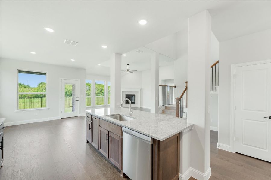 Kitchen island with granite countertop and sink, open to living area with hardwood floors and staircase nearby. Kitchen island with granite countertop and sink, open to living area with hardwood floors and staircase nearby.
