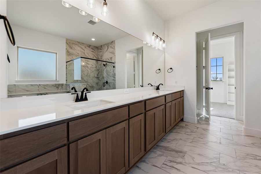 Bathroom with healthy amount of natural light, light marble finish flooring, double vanity, and a marble finish shower