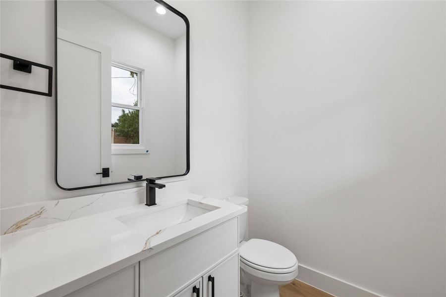 A secondary bathroom features modern fixtures, contemporary lighting, and a clean minimalist design with quartz surfaces and designer hardware. The neutral finish palette continues the home’s cohesive architectural style throughout.