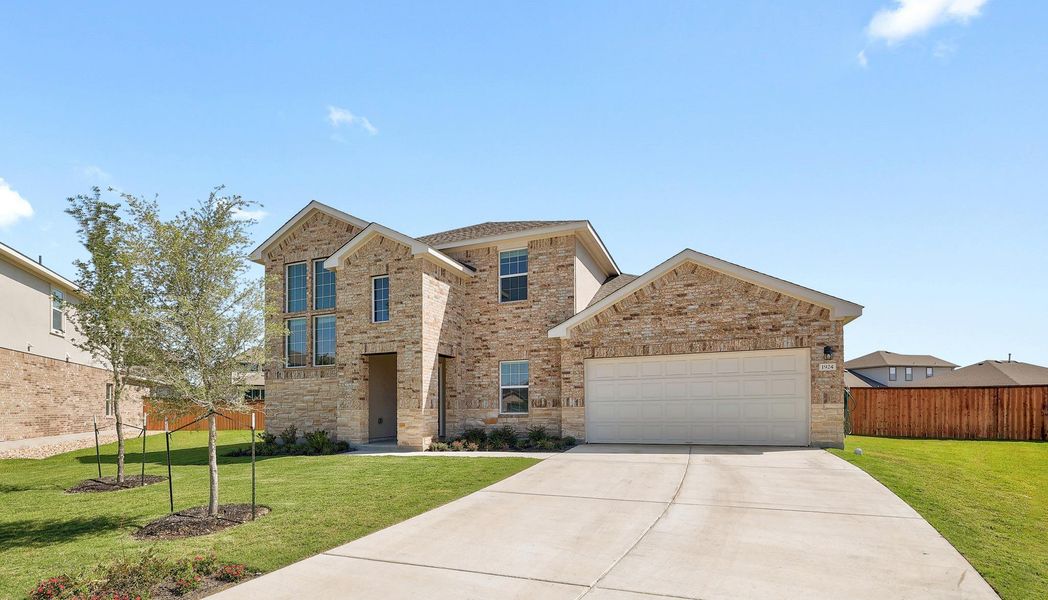 Two-story residence featuring a brick and stone facade, an attached garage, a concrete driveway, a manicured front lawn, and visible rear fencing Two-story residence featuring a brick and stone facade, an attached garage, a concrete driveway, a manicured front lawn, and visible rear fencing