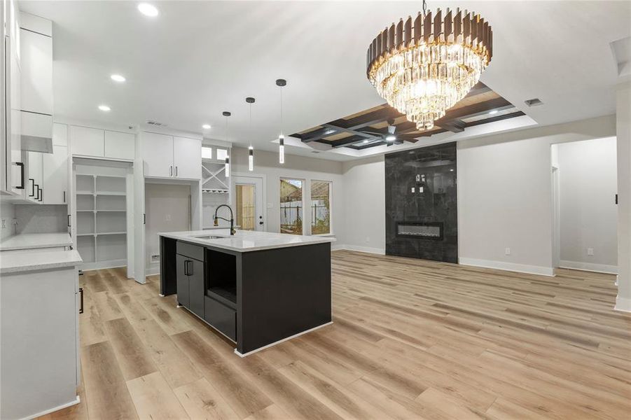 Kitchen with white cabinets, dark cabinets, a center island with sink, light stone counters, and coffered ceiling