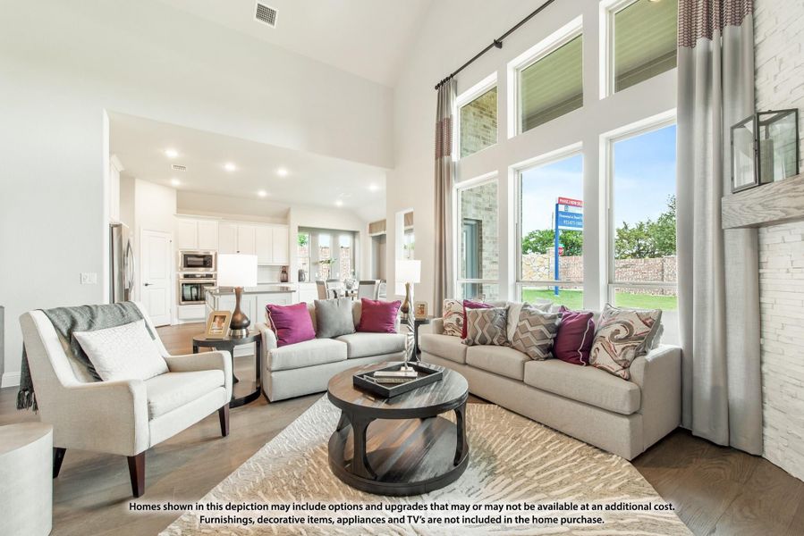 Open-concept living room with two-story windows, hardwood floors, and view into kitchen