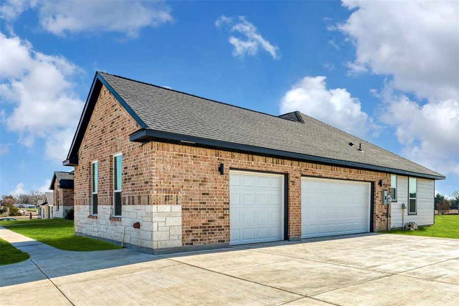 View of side of home with brick siding, concrete driveway, a shingled roof, and a garage