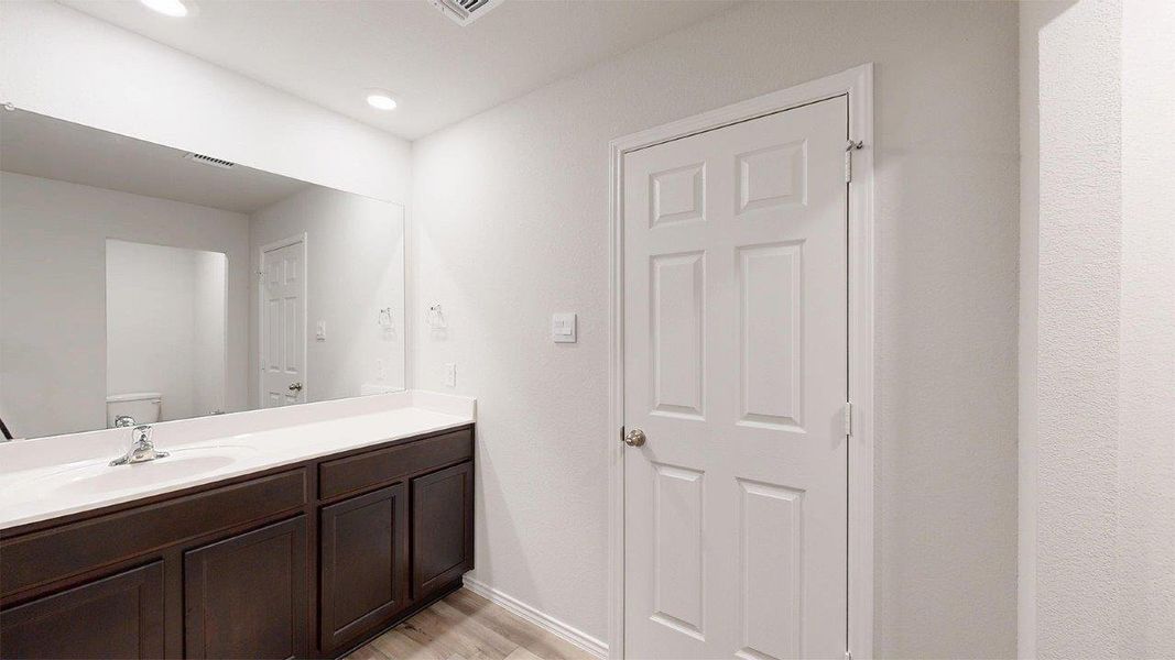 Bathroom vanity featuring dark wood-finish cabinetry, a white countertop with an integrated sink, and a large wall-mounted mirror Bathroom vanity featuring dark wood-finish cabinetry, a white countertop with an integrated sink, and a large wall-mounted mirror