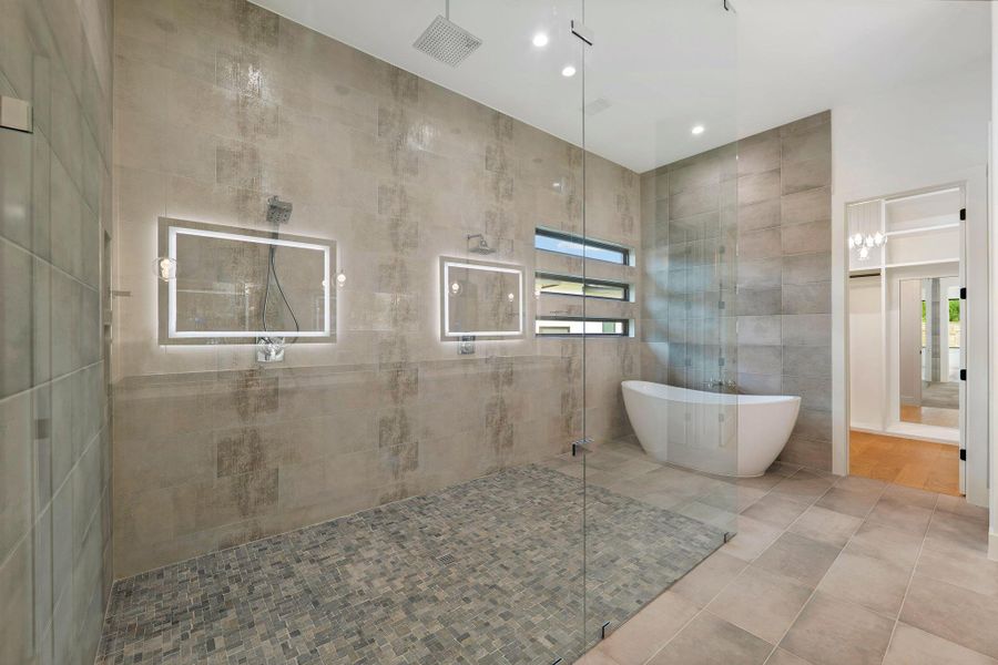 Spacious bathroom featuring a frameless glass shower enclosure with dual shower heads, a freestanding soaking tub, and illuminated vanity mirrors