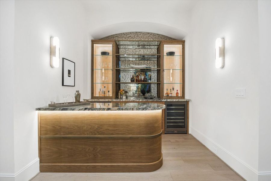 [Wet Bar] A striking custom wet bar with curved wood-front seating features Italian marble, and dual beverage refrigerators, anchored by an illuminated display wall with glass shelving—perfectly designed for sophisticated entertaining.