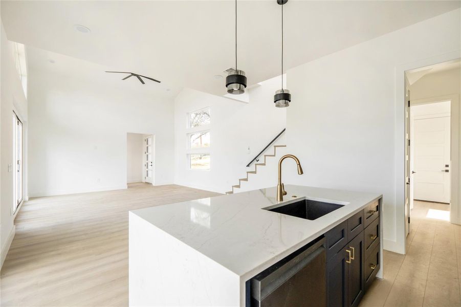 Kitchen with light stone countertops, a kitchen island with sink, light wood-style floors, stainless steel dishwasher, and open floor plan