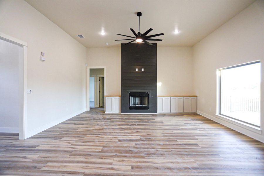 Unfurnished living room with a large fireplace, light wood finished floors, ceiling fan, and recessed lighting