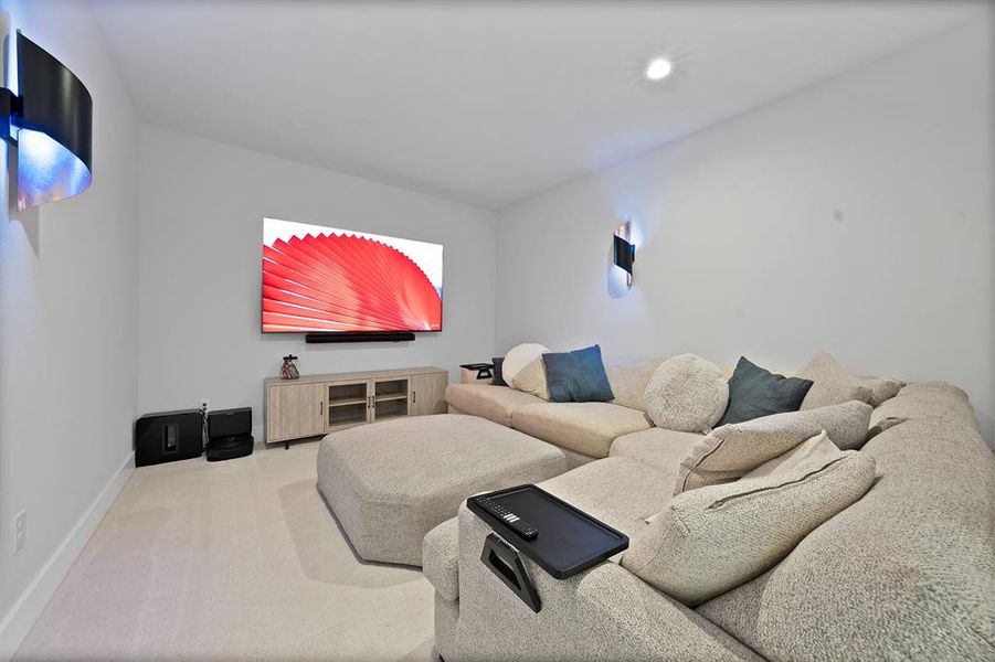 Carpeted entertainment area featuring white walls, a mounted television, two wall sconces, and a built-in media console with glass panel doors Carpeted entertainment area featuring white walls, a mounted television, two wall sconces, and a built-in media console with glass panel doors