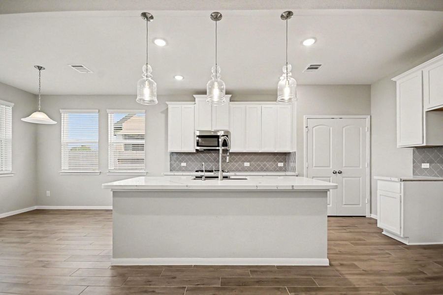 Bright and spacious kitchen featuring sleek white cabinetry, a large central island with modern pendant lighting, and elegant tile backsplash. Perfect for entertaining and family gatherings.