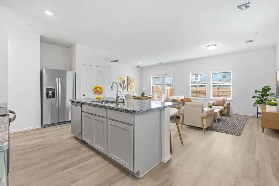 Open-concept living space featuring a central kitchen island with seating, stainless steel appliances, wood-finish flooring, and multiple windows for abundant natural light Open-concept living space featuring a central kitchen island with seating, stainless steel appliances, wood-finish flooring, and multiple windows for abundant natural light