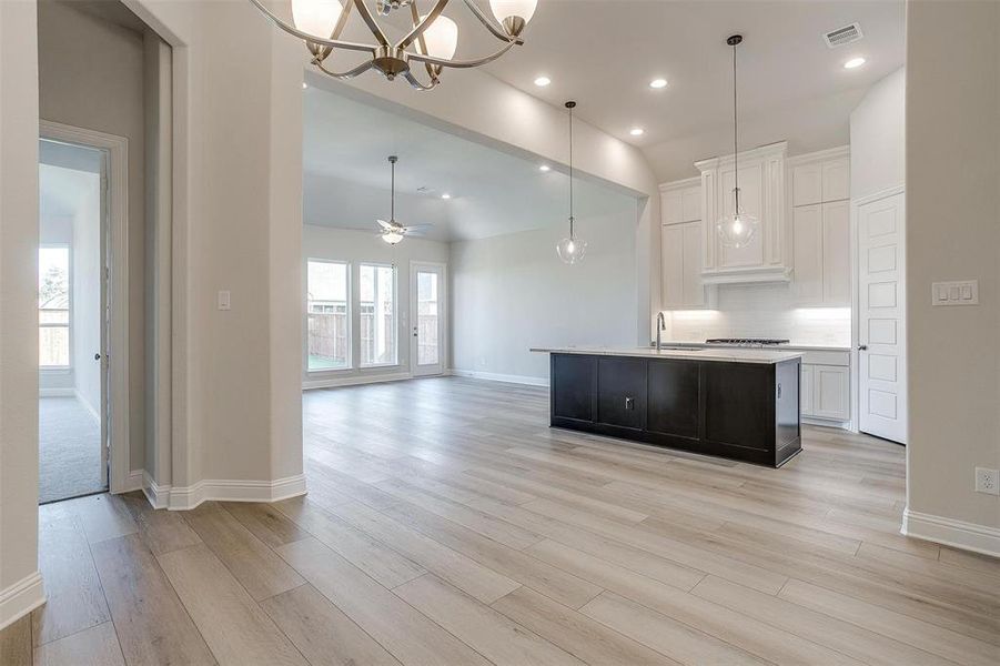 Kitchen with ceiling fan with notable chandelier, an island with sink, decorative light fixtures, light hardwood / wood-style floors, and white cabinetry