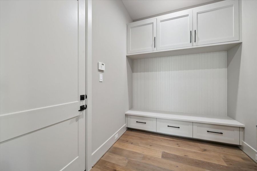 This mudroom is designed for both function and style, featuring built-in cabinetry above and below for ample storage. A custom bench with drawers provides a convenient spot for seating and organization, while beadboard detailing adds a touch of charm to the clean, modern design.
