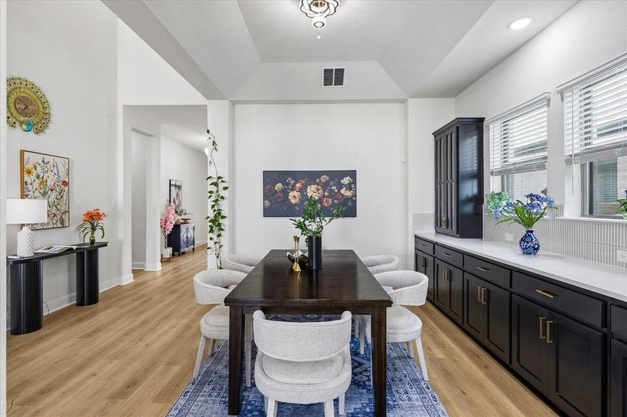 Dining area featuring wood-finish flooring, a recessed ceiling with decorative lighting, and a built-in buffet with dark cabinetry and light countertops Dining area featuring wood-finish flooring, a recessed ceiling with decorative lighting, and a built-in buffet with dark cabinetry and light countertops