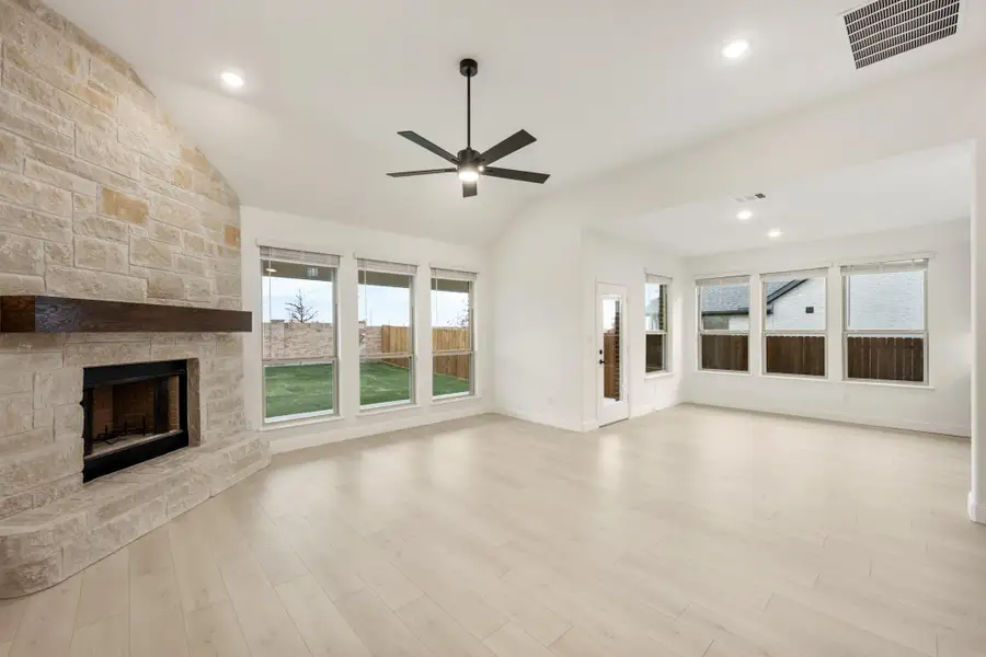 Open living room with floor-to-ceiling stone fireplace, vaulted ceiling, ceiling fan, and light wood floors Open living room with floor-to-ceiling stone fireplace, vaulted ceiling, ceiling fan, and light wood floors